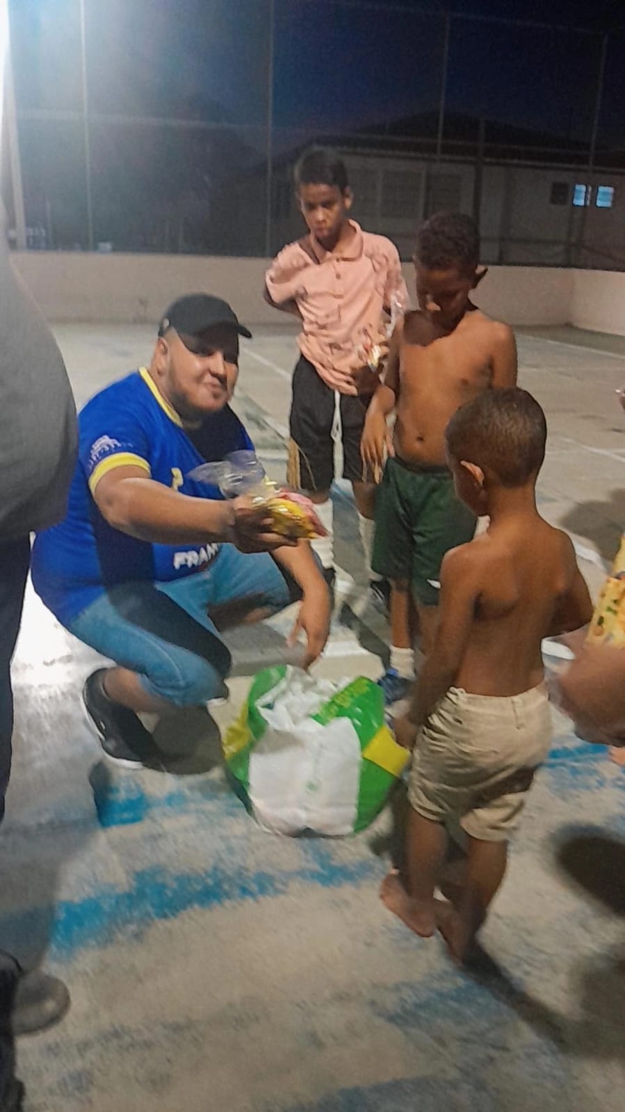 Thiago entrega um dos kits a uma criança da comunidade durante a ação de 2025