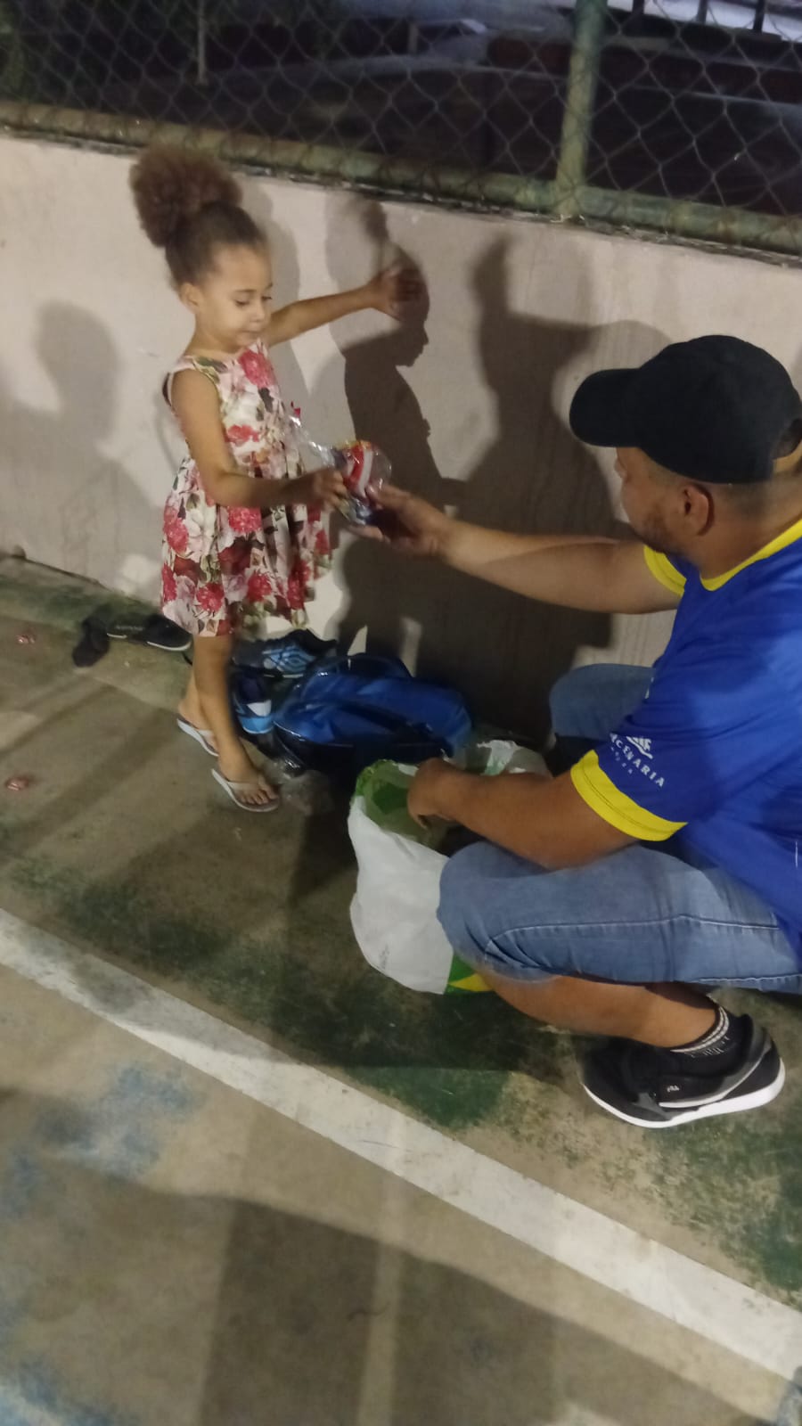 Thiago entrega um kit a uma criança vista de costas durante a ação comunitária de 2025
